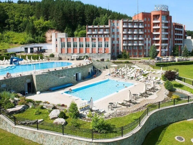 Spa resort with outdoor pools, sun loungers and a hotel building in a forested valley